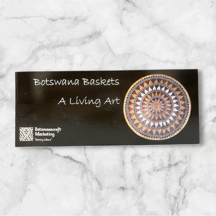 Book with 'Botswana Baskets: A Living Art' text and a decorative basket design on a marble background