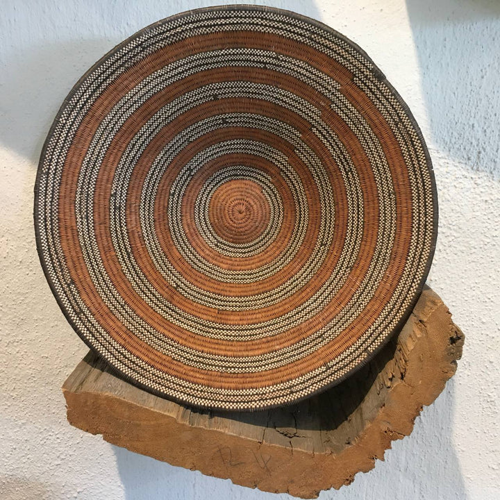 Round woven mat with concentric circle pattern on a wooden block against a light background