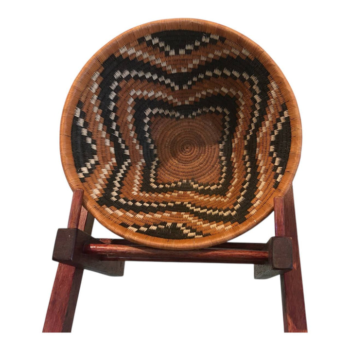 Woven basket with concentric circle pattern on a wooden stand against a white background