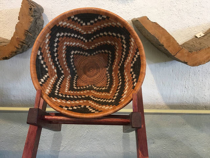 Woven basket with a geometric pattern on a wooden stand against a textured wall.
