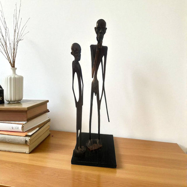 Two black figurines on a wooden surface with books and a vase in the background.