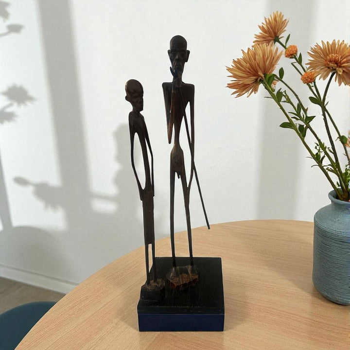 Three black figurines on a stand next to a vase with flowers on a wooden table.