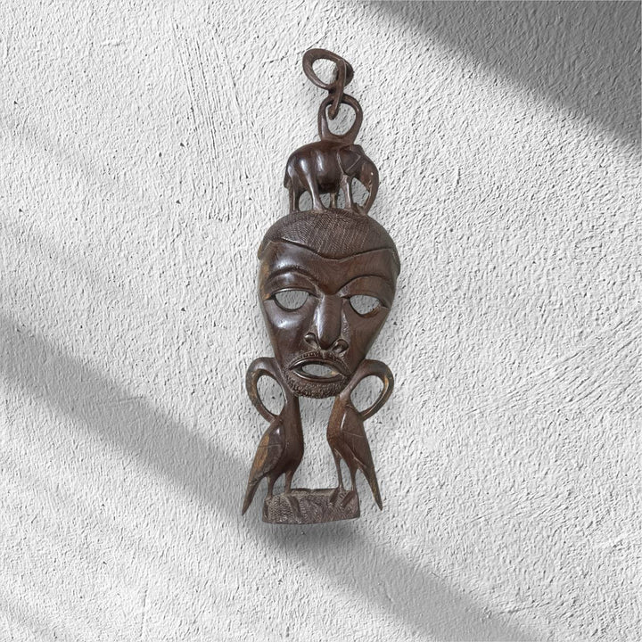 Decorative wooden mask hanging on a textured white wall