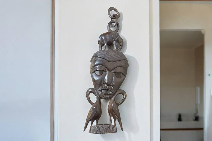 Decorative wooden mask hanging on a textured white wall