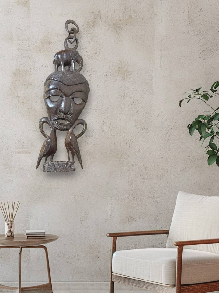 Decorative wall sculpture of a face on a textured wall with a chair and plant in the foreground.