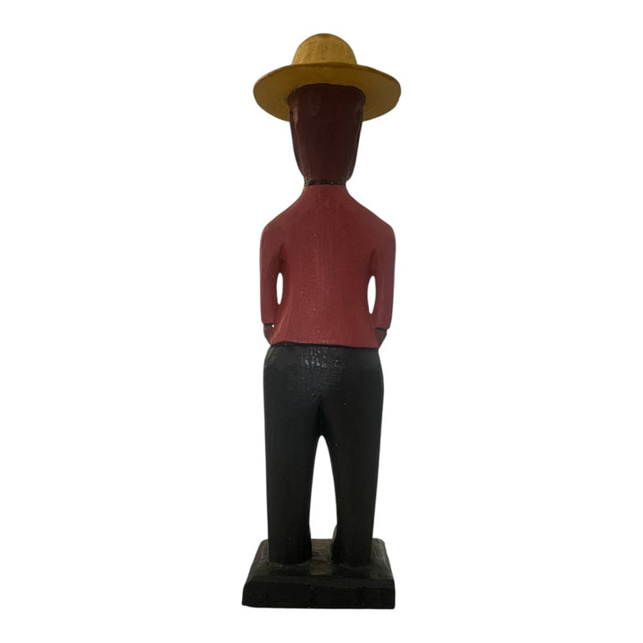 Wooden figurine of a person wearing a yellow hat and red shirt on a white background