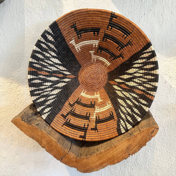 Woven basket with geometric pattern on a wooden stand against a white background