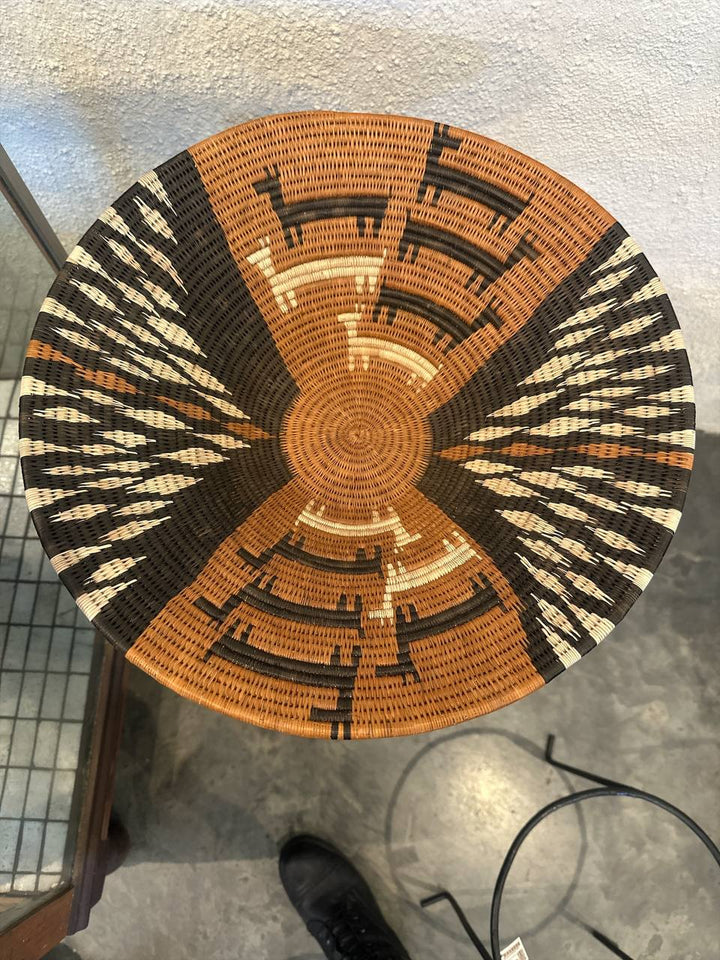 Woven basket with black, orange, and white pattern on a concrete floor.