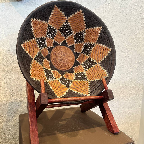 Woven basket with geometric pattern on a wooden stand against a textured wall.
