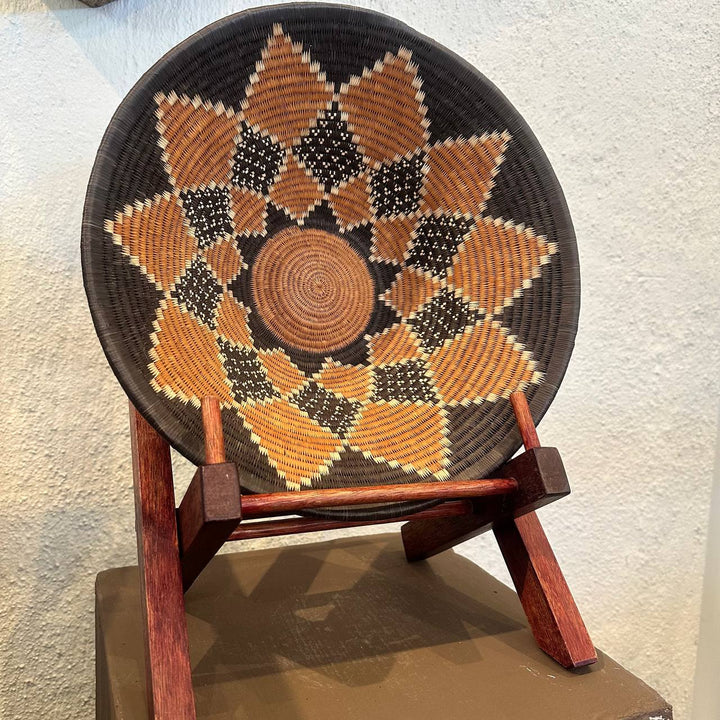Woven basket with geometric pattern on a wooden stand against a textured wall.