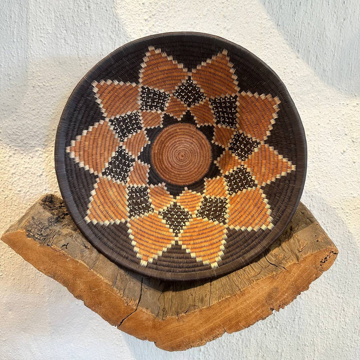 Woven basket with geometric pattern on a wooden stand against a light background