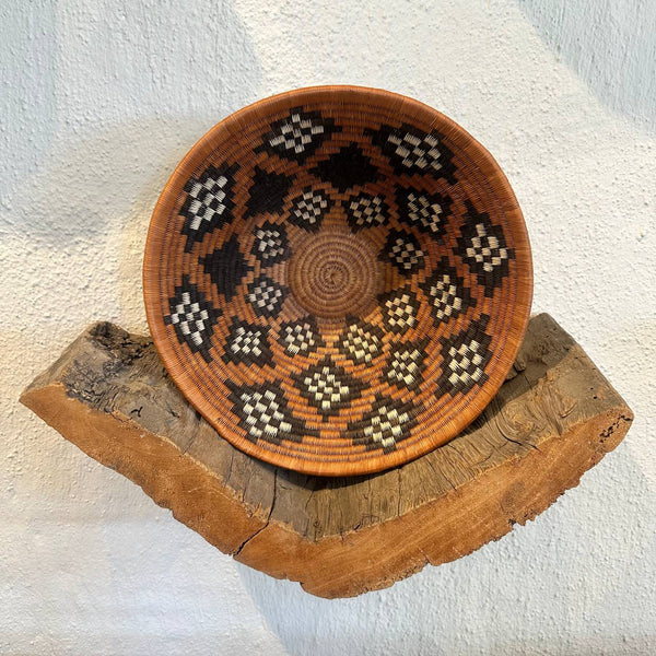 Decorative woven bowl with geometric pattern on a wooden stand against a white background