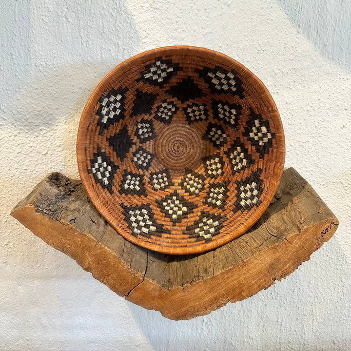 Decorative woven bowl with geometric pattern on a wooden stand against a white background