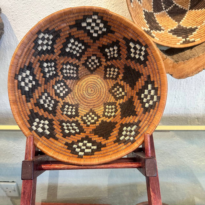 Woven basket with geometric pattern on a wooden stand against a neutral background
