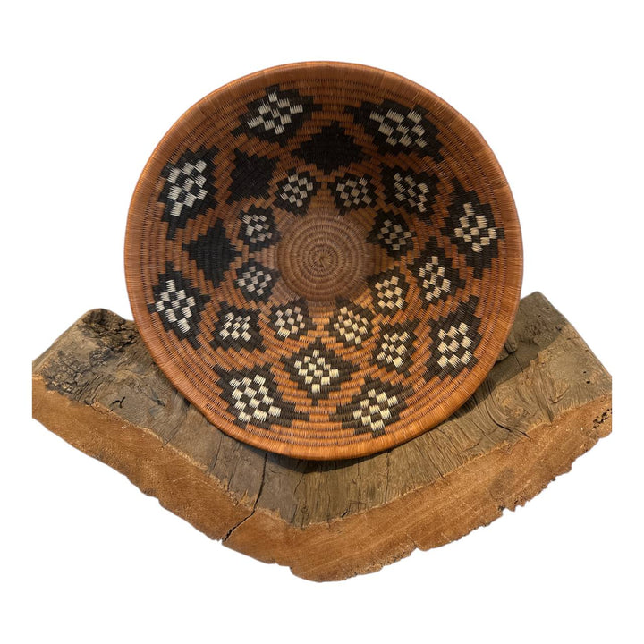 Woven basket with geometric pattern on a wooden stand against a white background