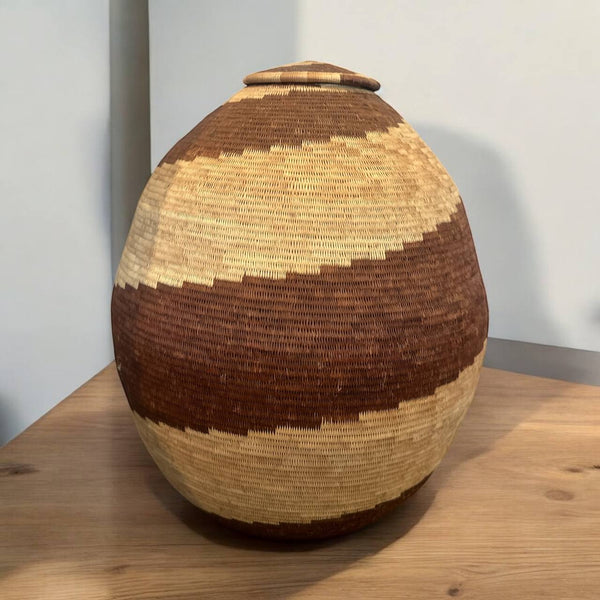 Woven basket with a lid on a wooden surface against a plain background