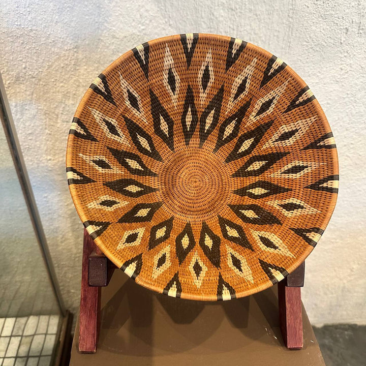 Decorative woven basket with a geometric pattern on a stand against a neutral background
