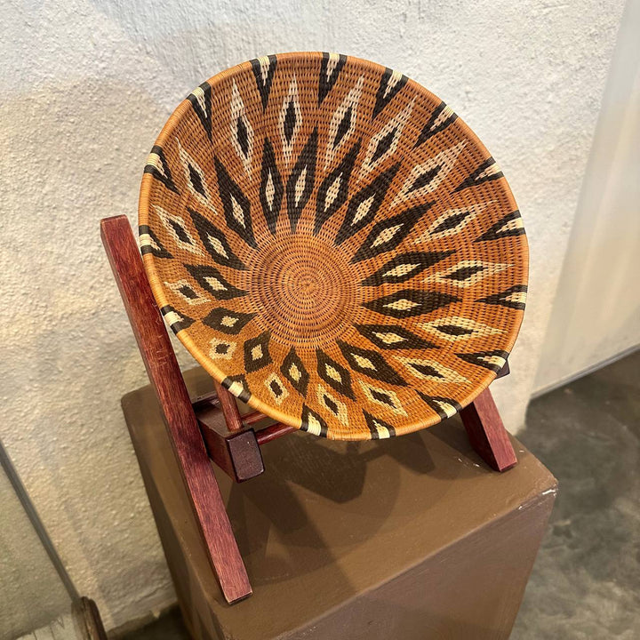 Woven basket with geometric pattern on a wooden stand against a neutral background