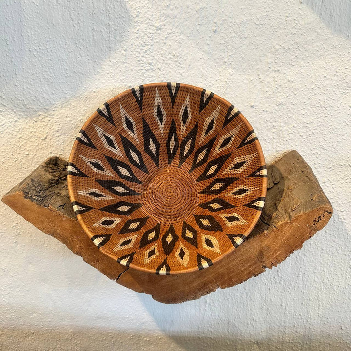 Decorative woven bowl with geometric pattern on a wooden stand against a white background