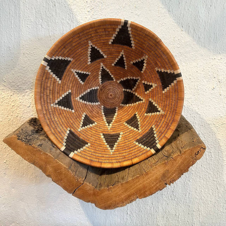 Woven basket with geometric pattern on a wooden stand against a white background