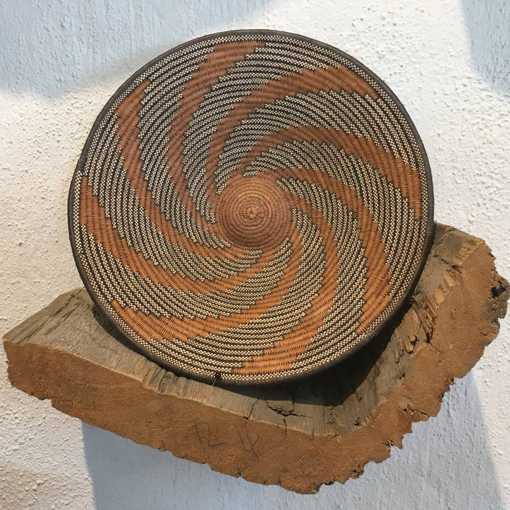 Woven basket with spiral pattern on a wooden block against a white wall